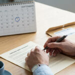 Une personne signe un contrat de crédit consommation sur un bureau avec un calendrier marqué au 14 septembre.